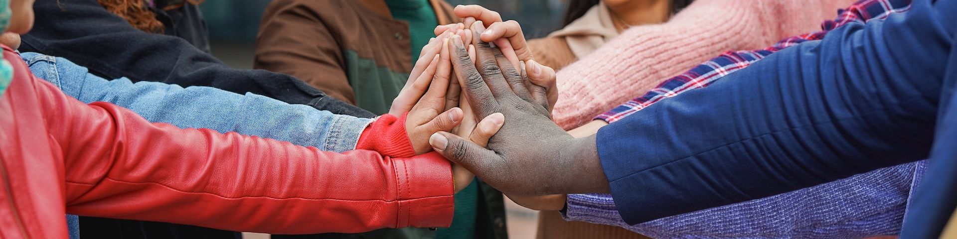 Eine Gruppe junger Menschen steht im Kreis und verschränkt die Hände in der Mitte.