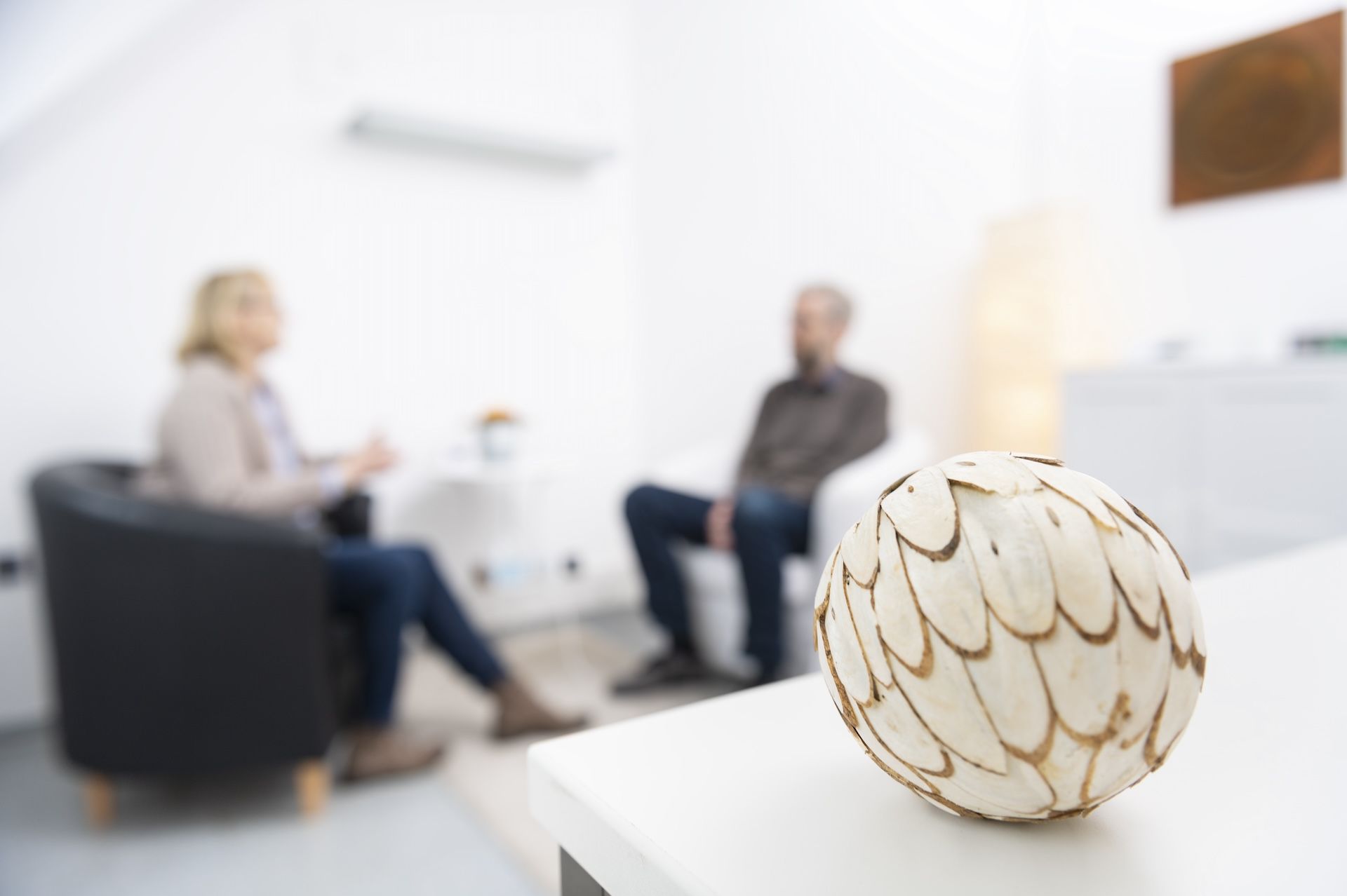 Blick in ein helles Gesprächszimmer. Im Hintergrund sind unscharf zwei Personen in Sesseln zu sehen, im Vordergrund ist eine Deko-Kugel.