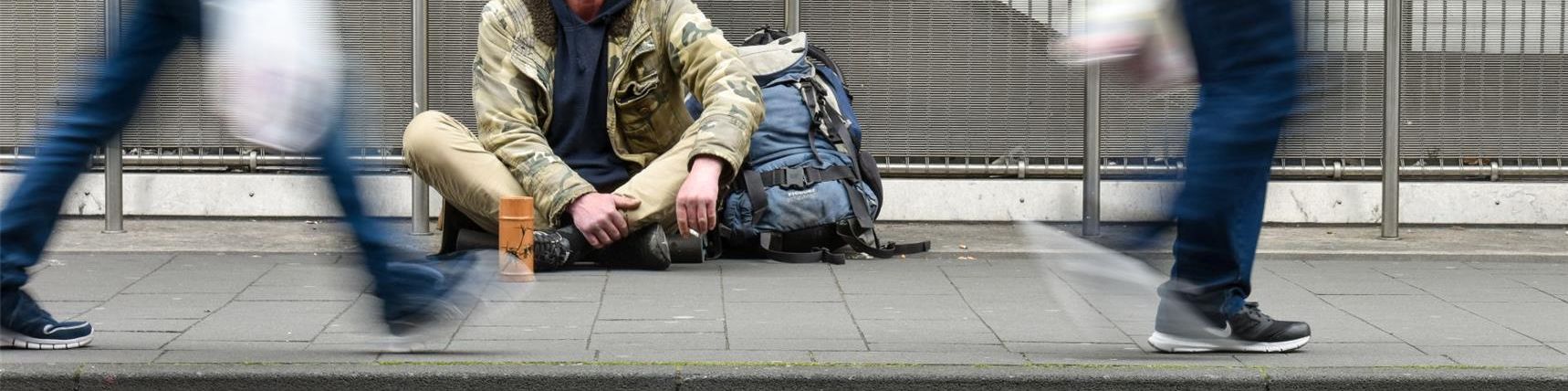 ein Obdachloser auf der Straße schaut zwei vorbeigehende Passanten an